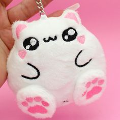 a hand holding a white stuffed animal keychain with pink paw prints on it