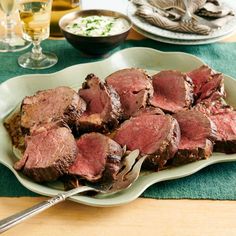 a plate full of sliced meat on top of a table with wine glasses and utensils