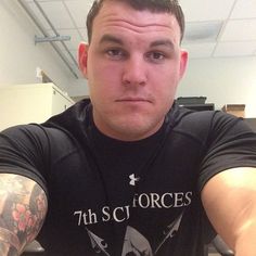 a man with tattoos on his arms sitting in front of a computer desk and looking at the camera