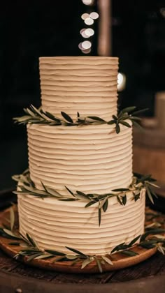 a three tiered white cake with green leaves on the top is sitting on a wooden table