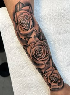 a black and grey rose tattoo on the arm with an arrow in the center, surrounded by other roses