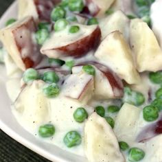 a white plate topped with peas and meat covered in sauce on top of a table