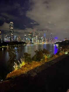 the city skyline is lit up at night with lights reflecting in the water and clouds