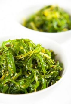 two white bowls filled with green vegetables on top of a table