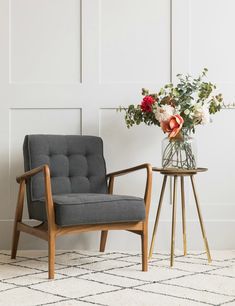 a chair and vase with flowers in it on a rug next to a white paneled wall