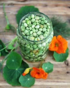 a glass jar filled with green beans next to some orange flowers on a wooden table