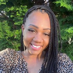 a smiling woman with braids on her head and leopard print shirt in front of trees