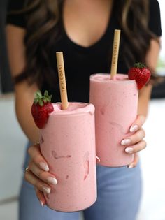 two women holding pink smoothies with strawberries on top and one has a straw in it