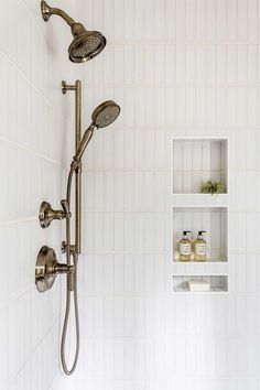 a shower head and hand shower in a white tiled bathroom with shelves on the wall