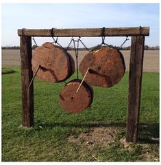 two pieces of wood hanging from chains on a wooden frame in the middle of a field