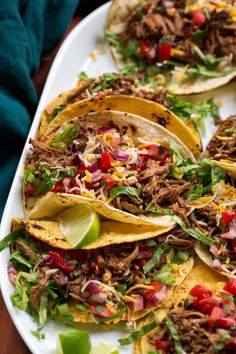 shredded beef tacos on a white platter with lime wedges