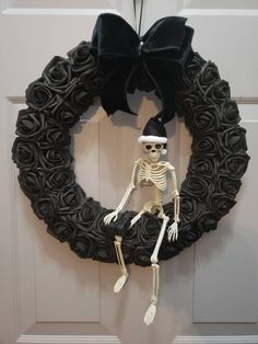 a wreath with a skeleton on it and a black bow hanging from the front door