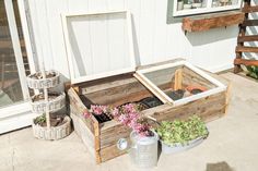 a wooden box filled with plants sitting on top of a cement floor next to a white building