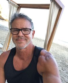 a man wearing glasses sitting on top of a beach