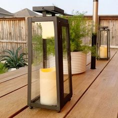 a lantern with a candle inside sitting on a wooden deck next to potted plants