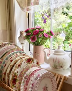 a bunch of plates that are sitting on a table next to a vase with flowers in it