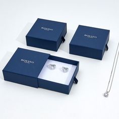 three blue boxes with diamond rings in them on a white surface next to a pair of scissors