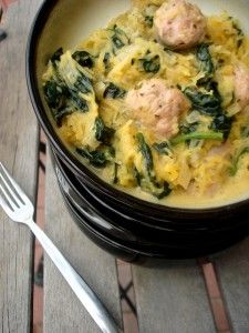 a bowl filled with meatballs and spinach on top of a wooden table