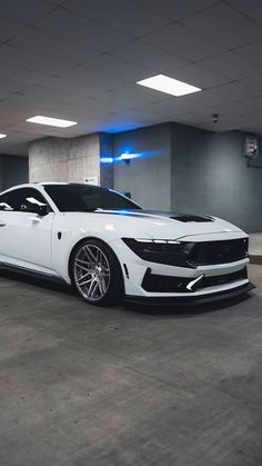 a white sports car parked in an empty parking garage with its hood up and lights on