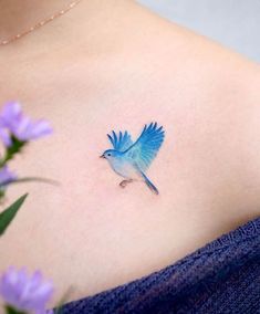 a small blue bird tattoo on the back of a woman's shoulder and chest