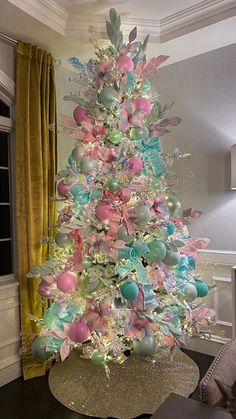 a decorated christmas tree with pink, blue and green ornaments on it in a living room