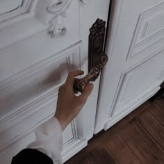 a person is holding the door handle on an ornately decorated white door with a key in it