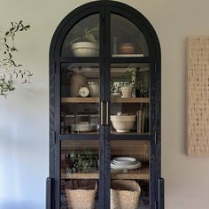 a black china cabinet with glass doors and wicker baskets on it's sides