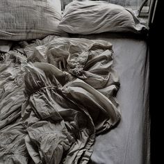 an unmade bed with several pillows and blankets on top of it, in black and white