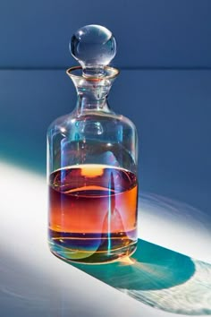 a glass decanter with liquid in it sitting on a table next to a shadow