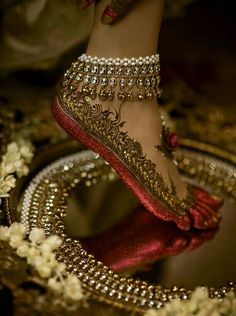 a woman's feet in gold and red shoes with jewels on the bottom, surrounded by flowers