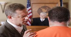 a man in an orange shirt and tie is talking to another man wearing an orange vest