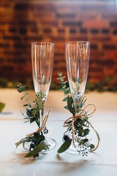 two champagne flutes with greenery and twine tied to each other on a table