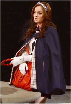 a woman is walking down the runway carrying a red purse and white gloves on her head