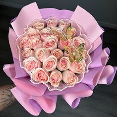 a bouquet of pink roses with a butterfly on the top is held by someone's arm