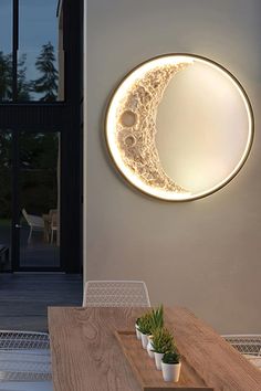 the moon is lit up on the wall above a table with two potted plants