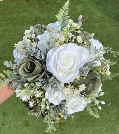 a bridal bouquet with white flowers and greenery is held by someone's hand