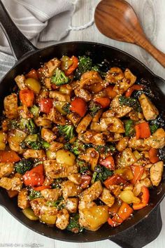 chicken and vegetable stir fry in a skillet with a wooden spoon on the side