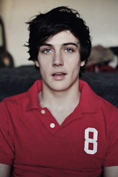 a young man in a red shirt looking at the camera with an intense look on his face