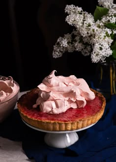 a strawberry pie with whipped cream on top and a bowl of flowers in the background