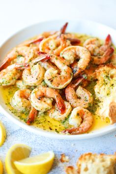 a white bowl filled with shrimp next to bread and lemon wedges on a table