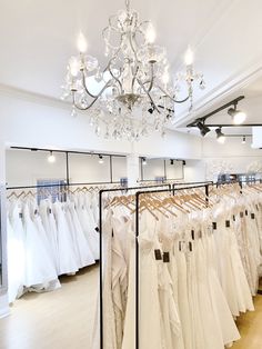 a room filled with lots of white dresses on display in front of a chandelier