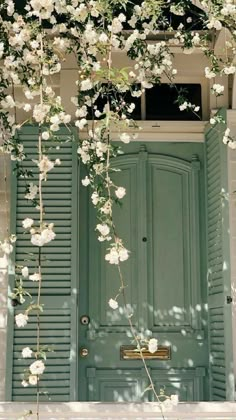 an open green door with white flowers growing on the side and below it is a window