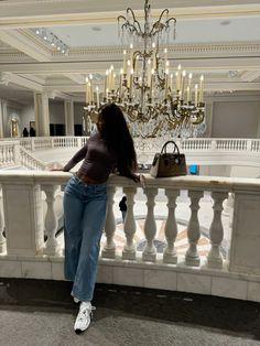 a woman leaning on a railing in front of a chandelier and handbag