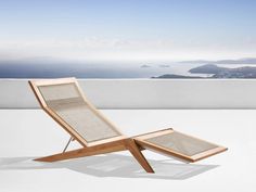 a wooden lounge chair sitting on top of a white floor next to an ocean view