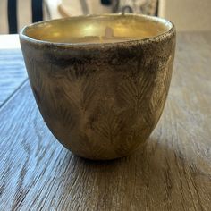 a candle that is sitting in a bowl on a table with a wood floor and chair behind it