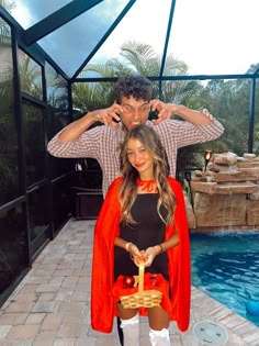 a man standing next to a woman in front of a pool with an umbrella over her head