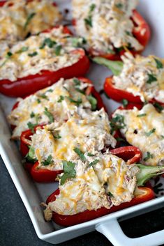 red peppers stuffed with chicken and cheese in a white dish on a black counter top