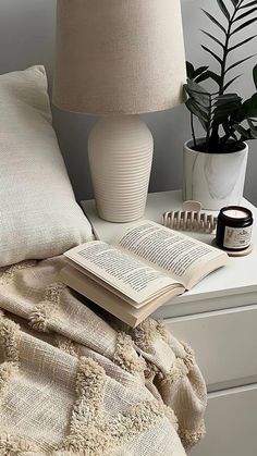 an open book sitting on top of a white table next to a lamp and potted plant