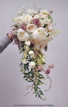 a bridal bouquet with white flowers and greenery is held by someone's hand