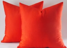 two bright orange pillows sitting on top of a white table next to eachother